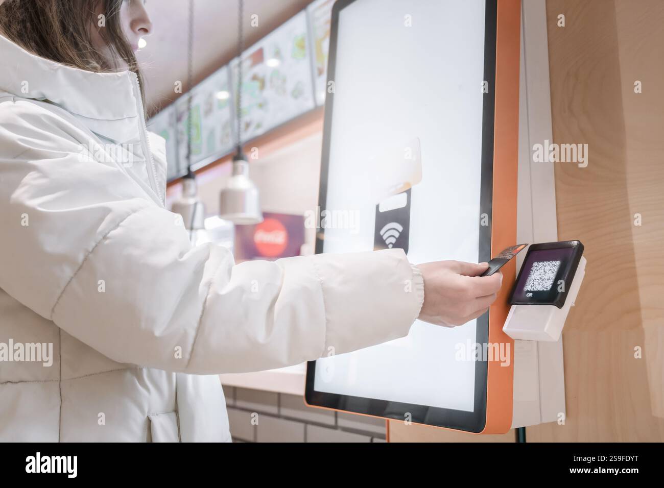 A woman pays with a card for a purchase through a touchscreen terminal for ordering food in a modern fast food restaurant, A satisfied customer is usi Stock Photo