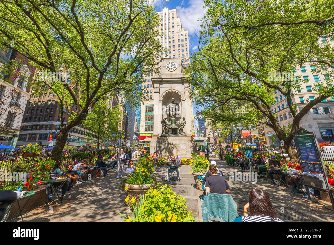 Lively atmosphere at Greeley Square Park in New York City with people relaxing under spring green trees. New York. USA. Stock Photo