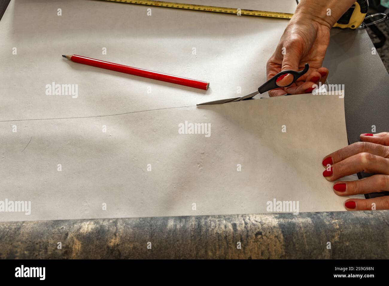 Cutting wallpaper before sticking it to the wall, scissors, measuring tape and pencil on the table, cutting wallpaper to size Stock Photo