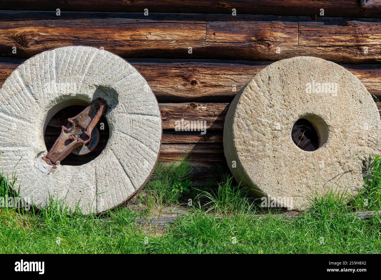 millstones-leaning-against-the-wall-of-an-old-wooden-house-stock-photo