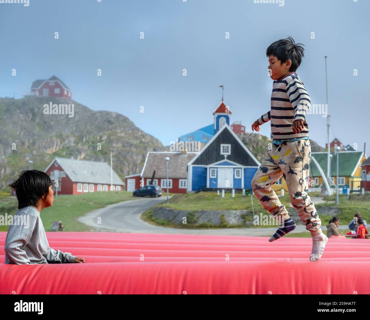 Two Inuit boys enjoy bouncing on an inflatable surface, surrounded by ...