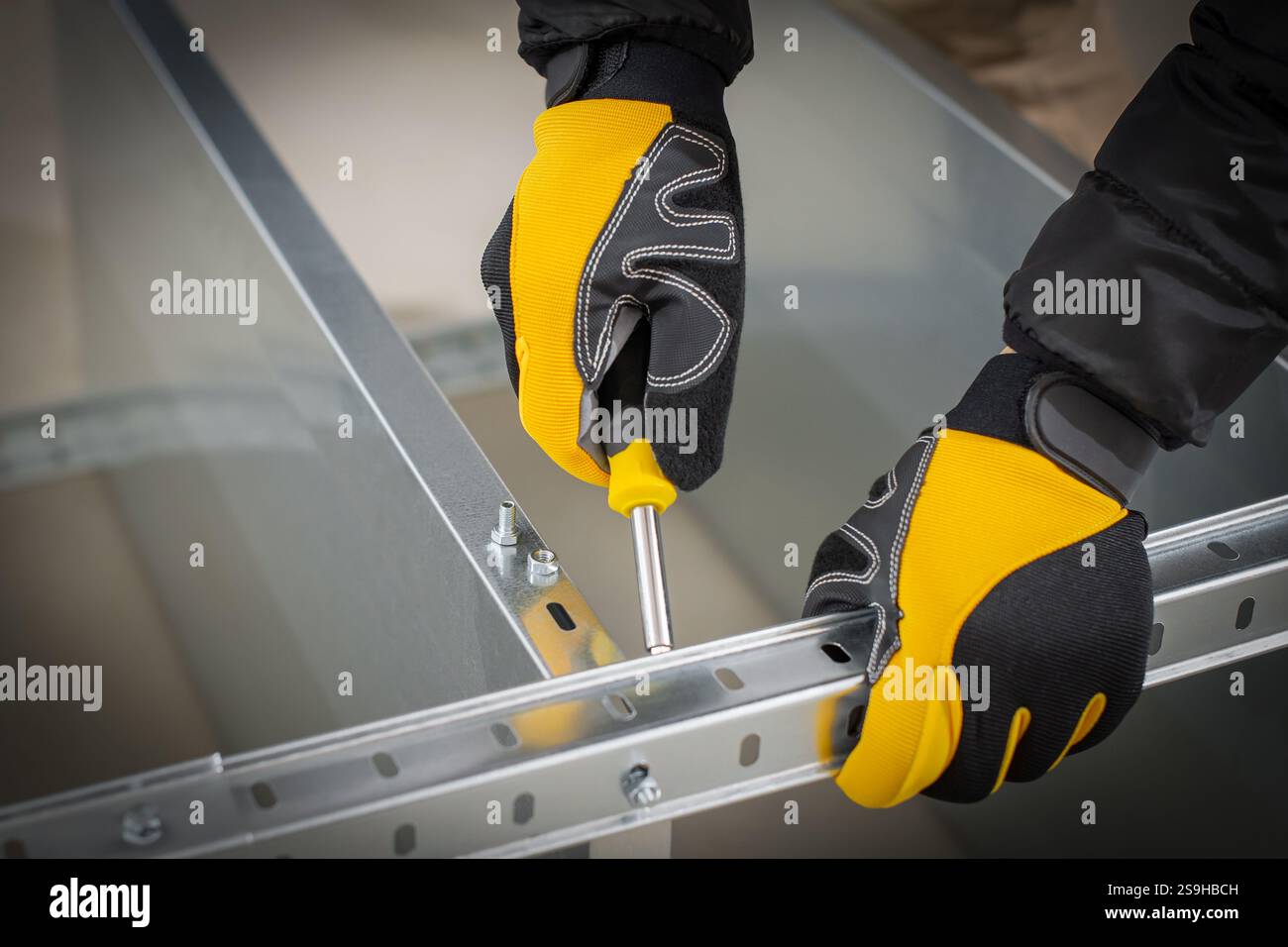 Worker hands in safety gloves mounting modular steel components with using screwdriver Stock Photo