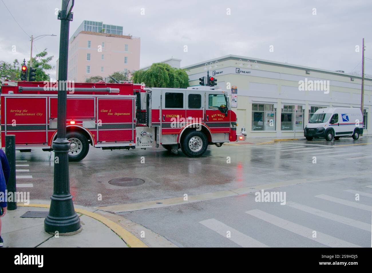 Large red and white fire truck left to right on the street. Postal delivery van on far side. Buildings and Palm trees in the background. Editorial Use Stock Photo