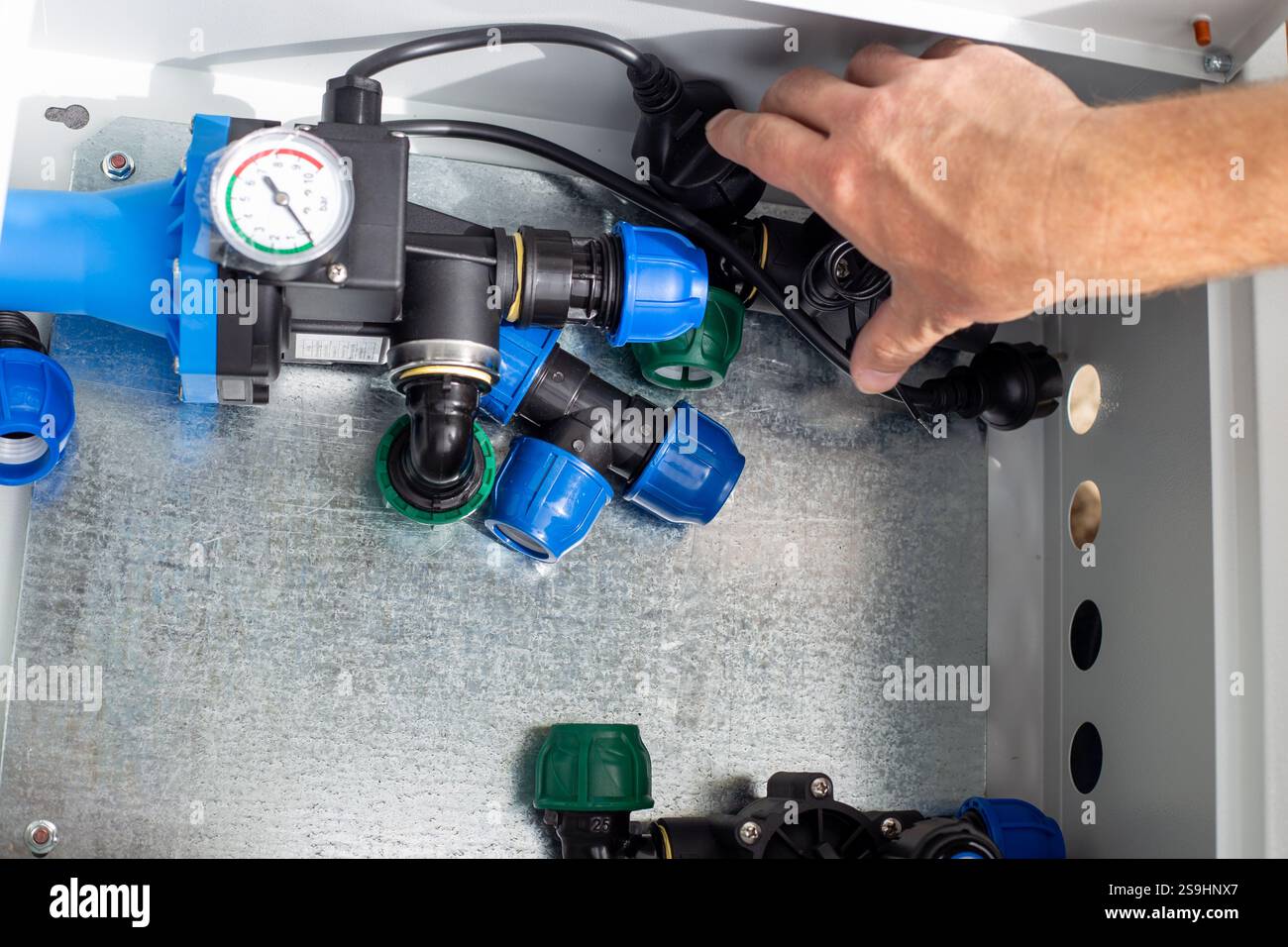 A man installs a drip irrigation system by placing automatic components in a metal box. Stock Photo