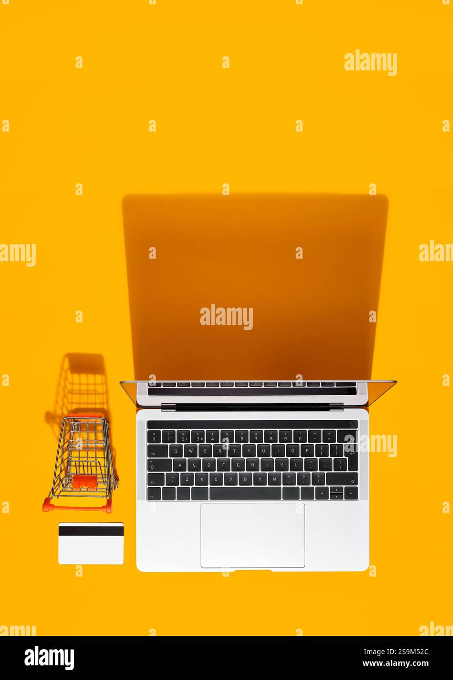 Laptop, shopping cart, and credit card arranged on a vibrant yellow background, representing online shopping and e-commerce Stock Photo