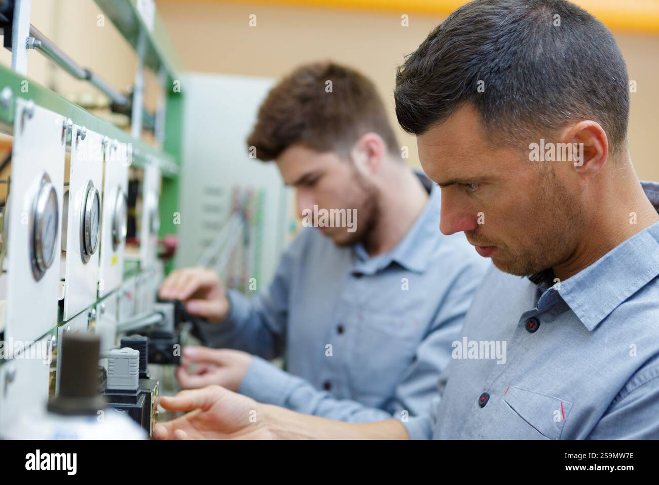two male technicians working on electrical panel with dials Stock Photo