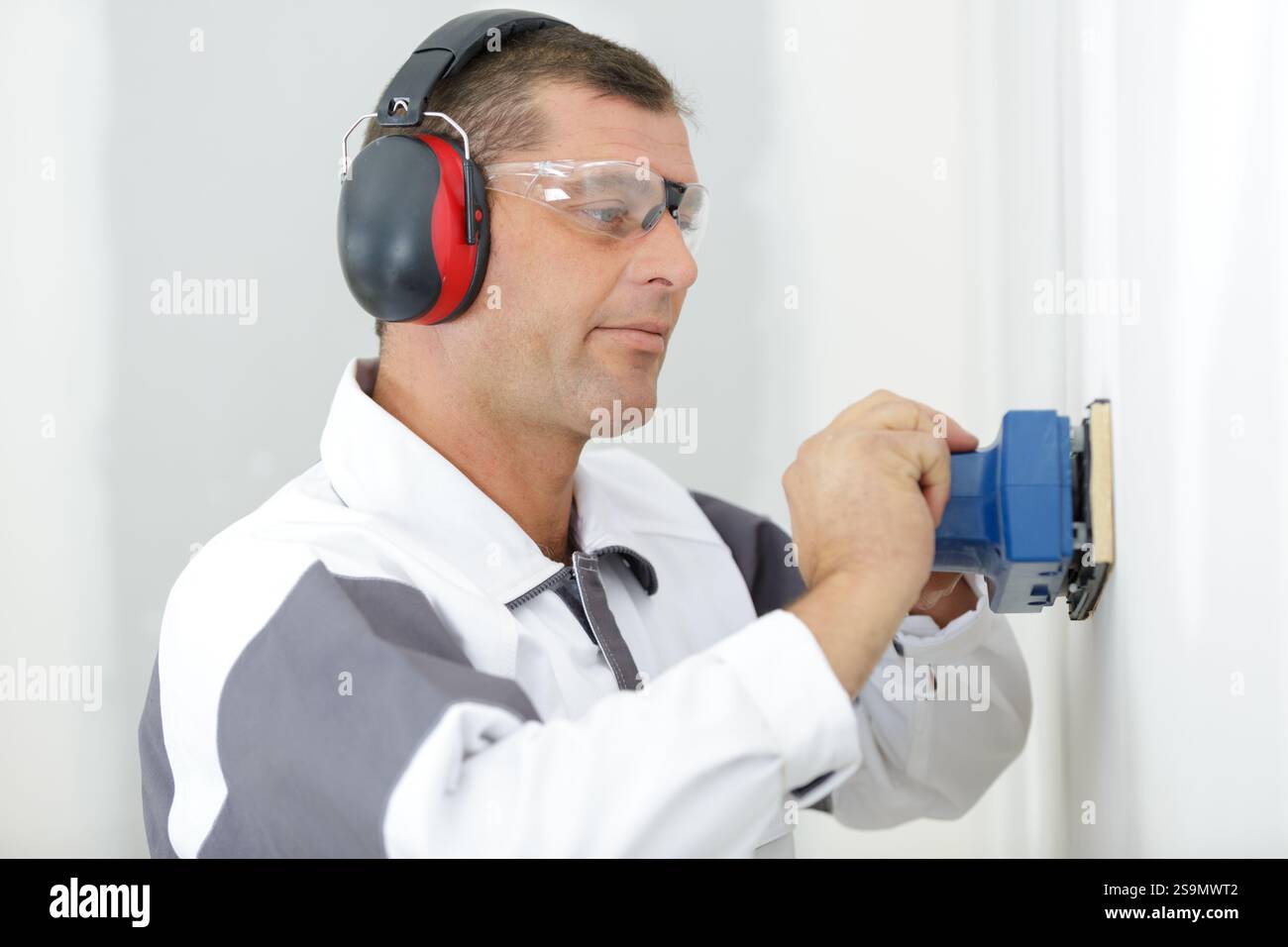 male builder using sander on plasterboard wall Stock Photo