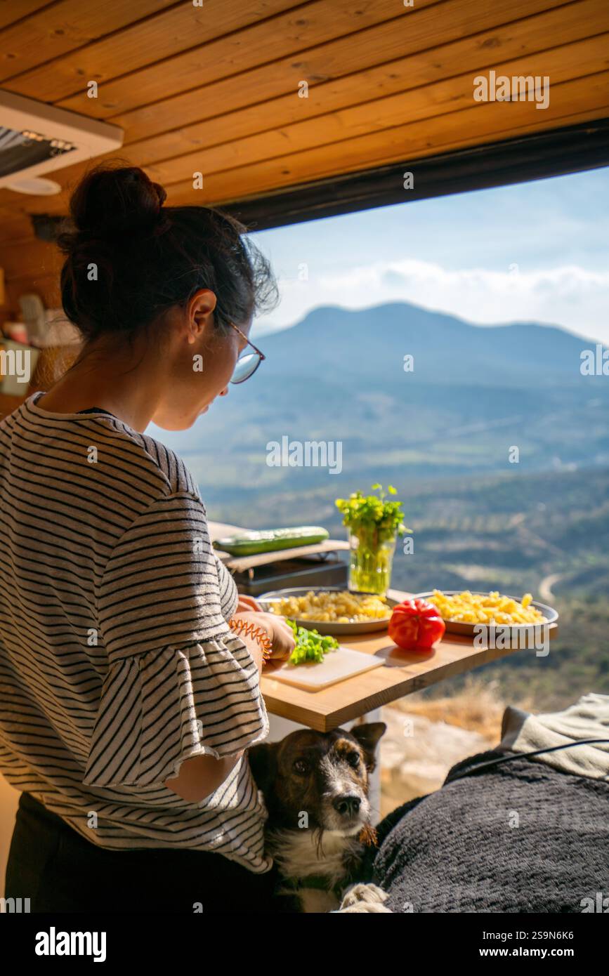Woman cooking inside a camper van with a dog with mountain view Stock Photo