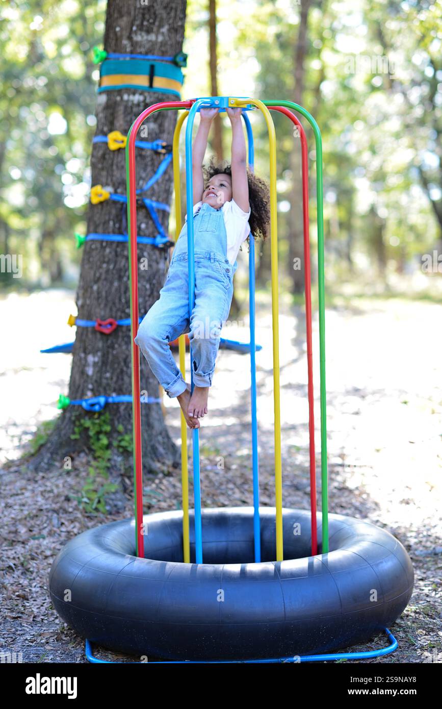 A child in overalls hangs on colorful playground bars over a tir Stock ...