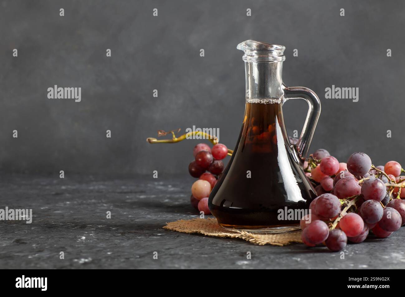Glass bottle of organic black grape balsamic vinegar made from fermented fresh grapes. Healthy organic food black fruit, selective focus Stock Photo
