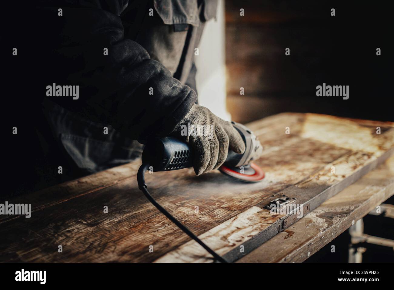 Craftsman using an angle grinder on wood, set in a rustic workshop environment Stock Photo