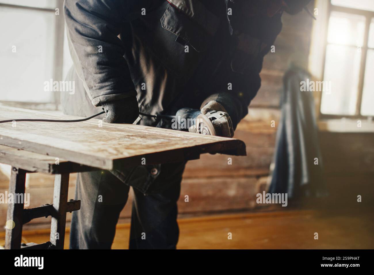 Carpenter working on a wood plank indoors, using a grinder in a workshop setting Stock Photo