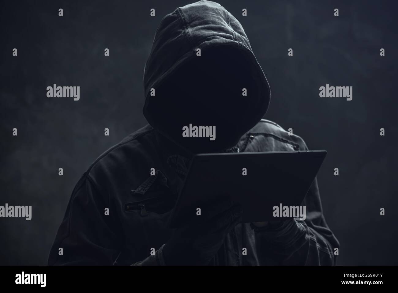 Hooded computer hacker using digital tablet, selective focus Stock Photo