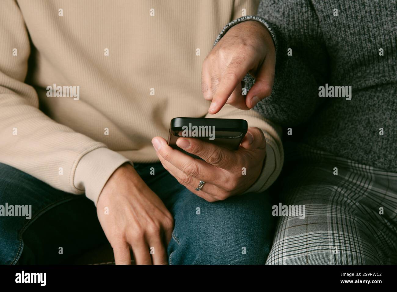 Man Using Something closeup of two men wearing casual clothes, sitting side by side on a ...