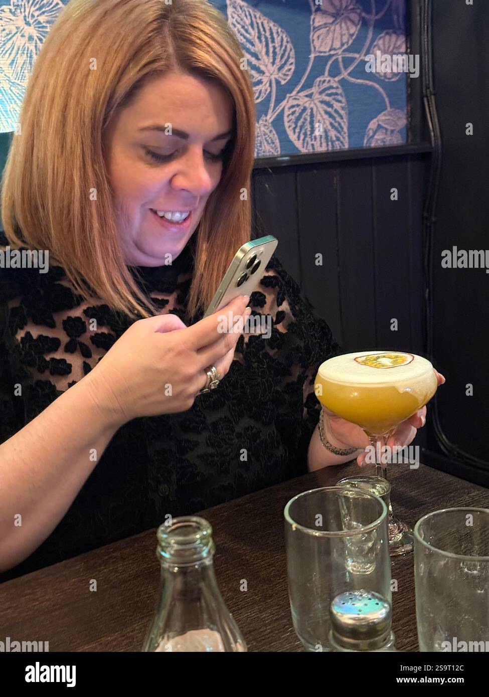 A woman photographing her cocktail to put it on social media - Smartphone Captured Stock Image