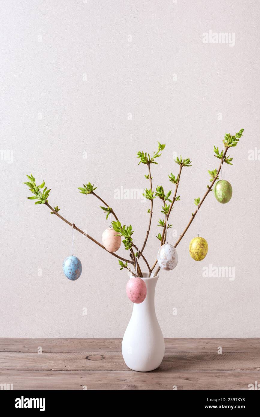 Vase with colorful Easter eggs hanging on spring branches, neutral background, minimal composition. Happy Easter concept. Stock Photo