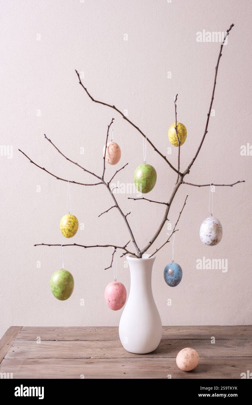 Painted Easter eggs on twigs in white vase, neutral background, minimal composition. Happy Easter decor. Stock Photo