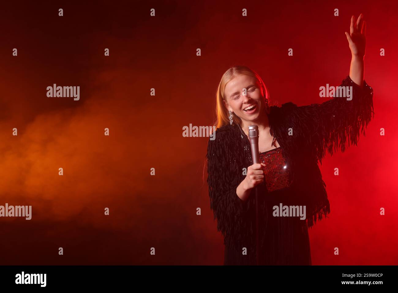 Beautiful singer performing on dark background with red light and smoke ...