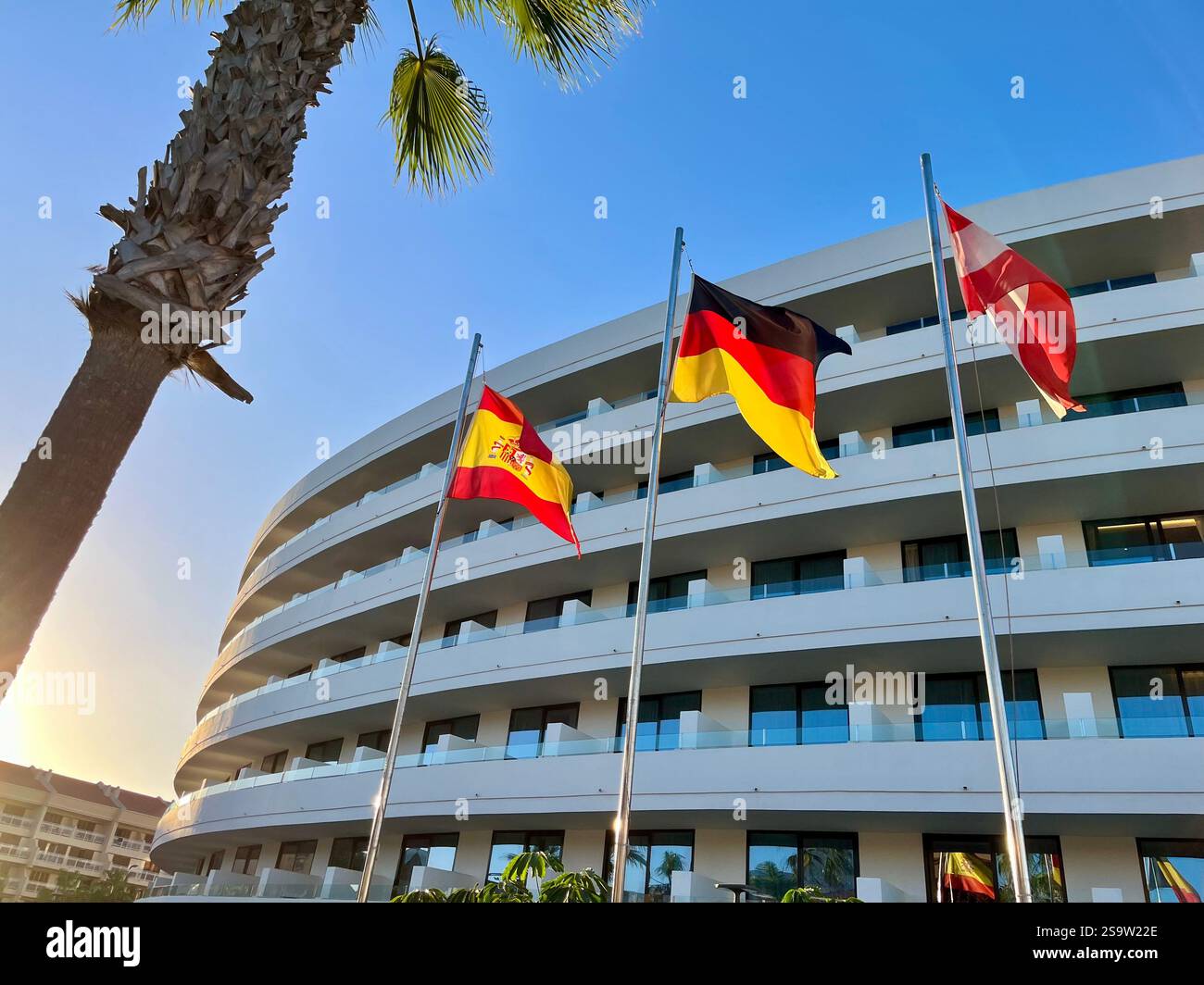 The flags of Spain, Germany, and Austria fluttering in the wind outside the refurbished Mediterranean Palace Hotel, part of the Mare Nostrum Resort. - Smartphone Captured Stock Image