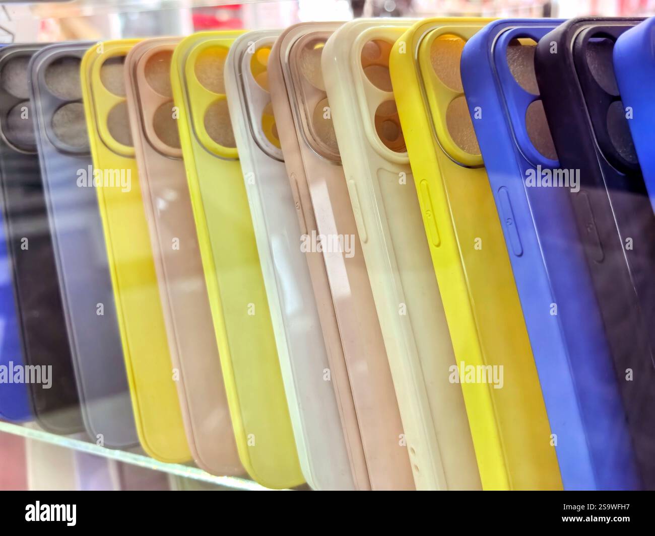 A vibrant collection of phone cases in various colors is arranged on a display shelf. The shop is bustling with activity as customers browse the lates Stock Photo