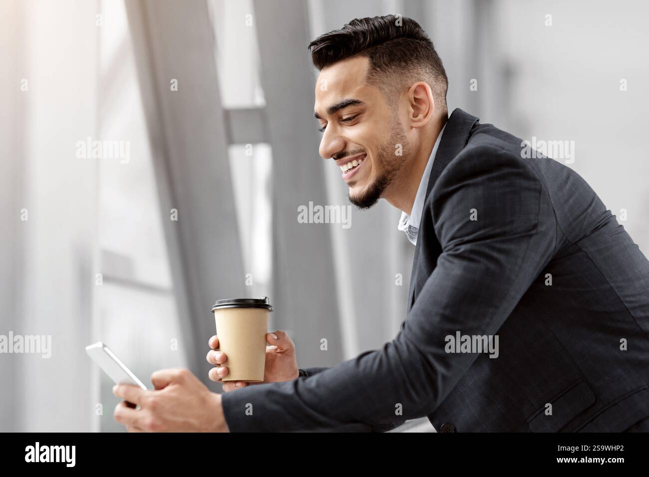 Happy Middle-Eastern Businessman Using Smartphone And Having Coffee While Waiting In Airport Stock Photo