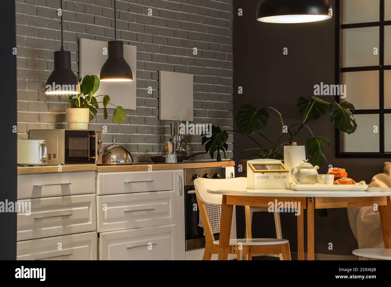 Interior of modern kitchen with glowing lamps, dining table and white ...
