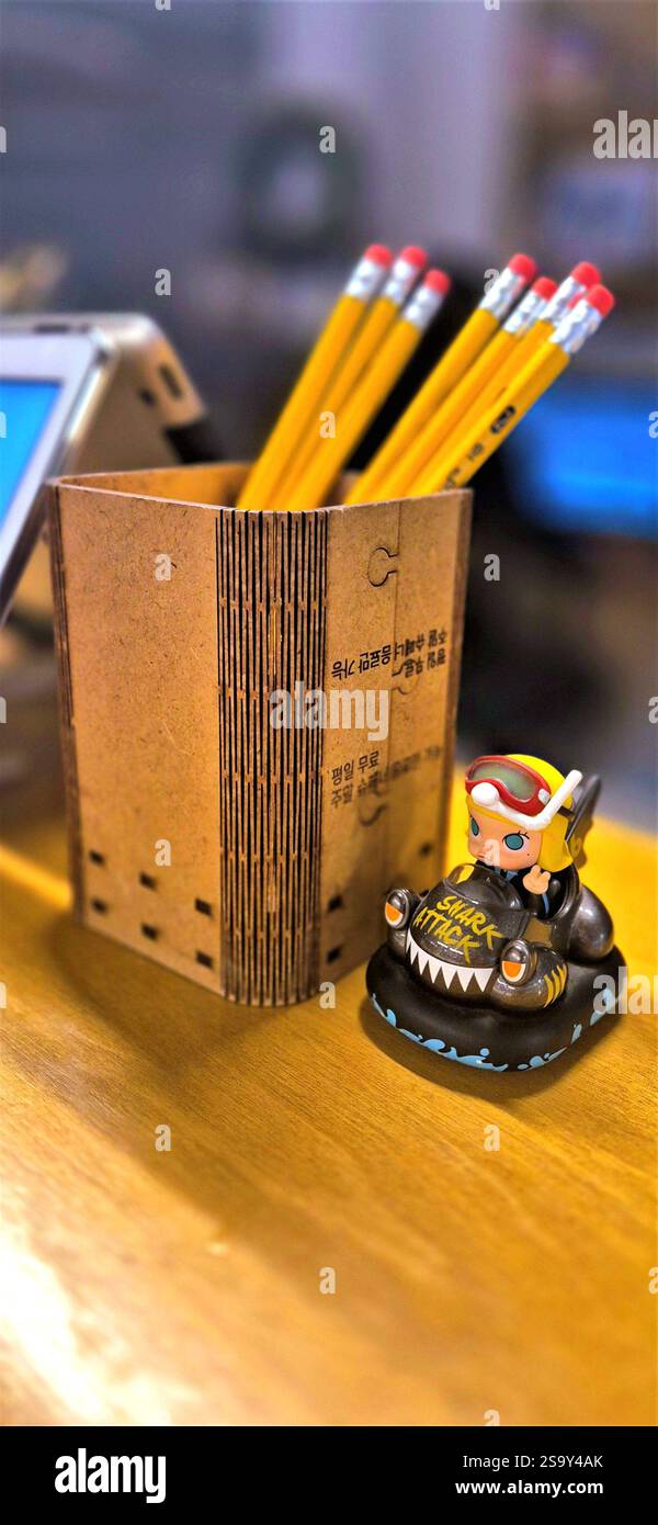 A pencil holder with a few pencils inside, next to a small figure on a wooden table in a cafe in Seoul - Smartphone Captured Stock Image