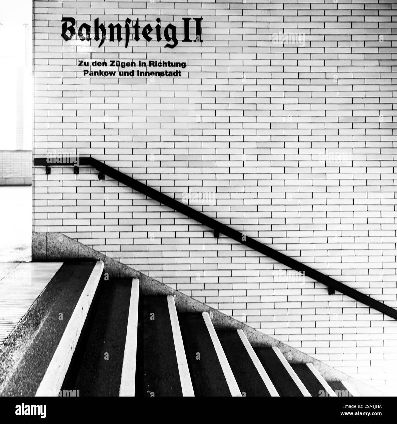 A black and white photograph of a staircase leading to a train platform ...
