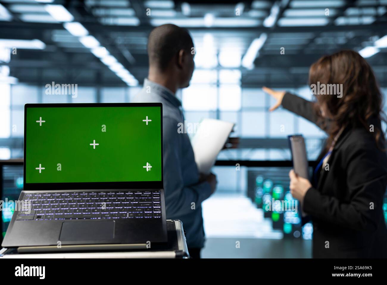 Green screen laptop in data center with programmers in blurry background employing machine learning models. Close up of chroma key notebook used by teamworking server room IT experts Stock Photo