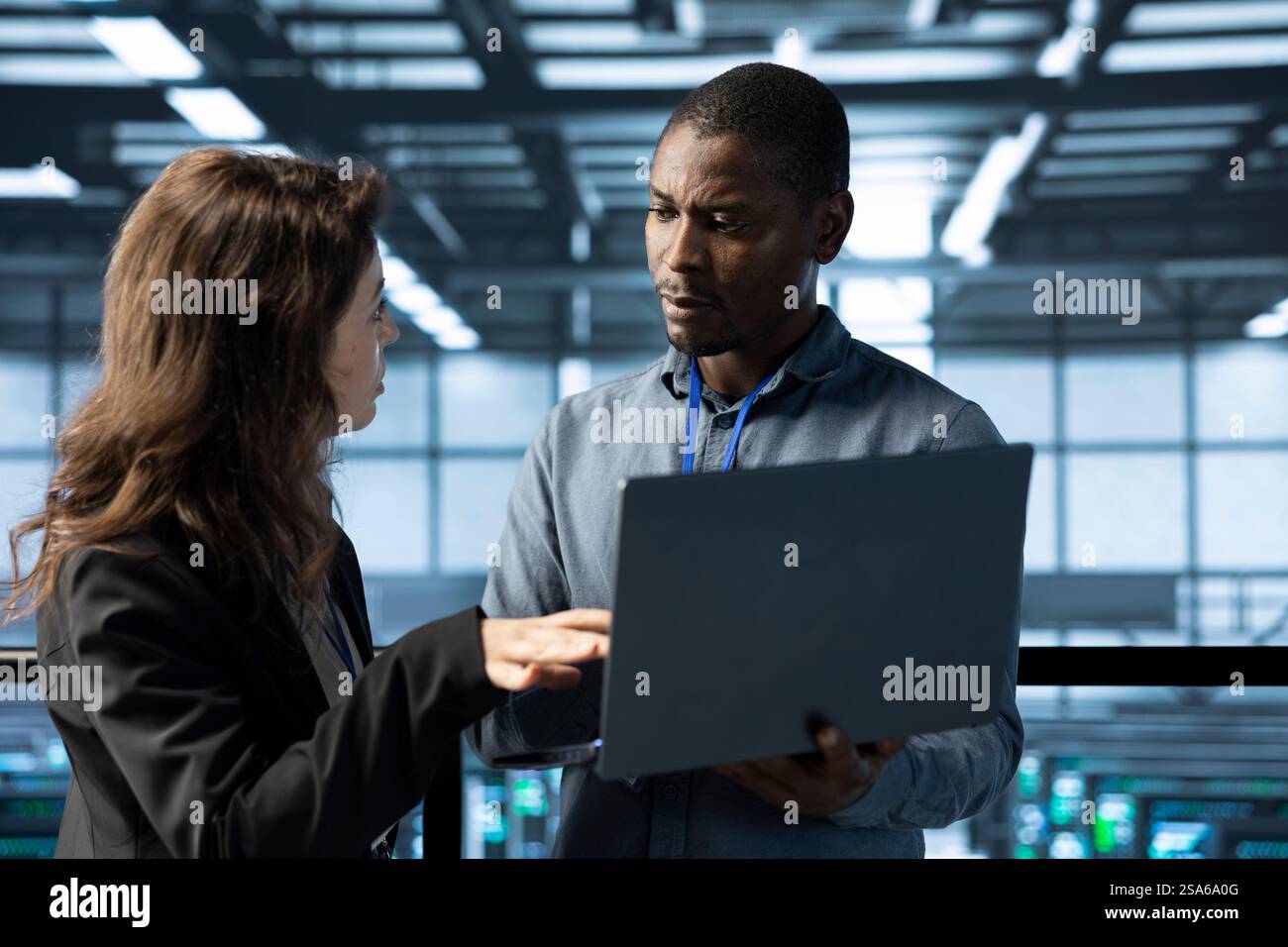 System administrators in data center using laptop, analyzing metrics, optimizing storage volumes. Server farm IT experts using notebook, talking, ensuring seamless operations Stock Photo