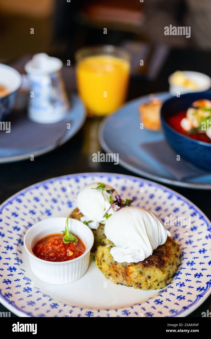 A beautifully plated dish featuring two poached eggs served on crispy potato cakes, accompanied by a small bowl of tomato salsa, creating a savory and Stock Photo