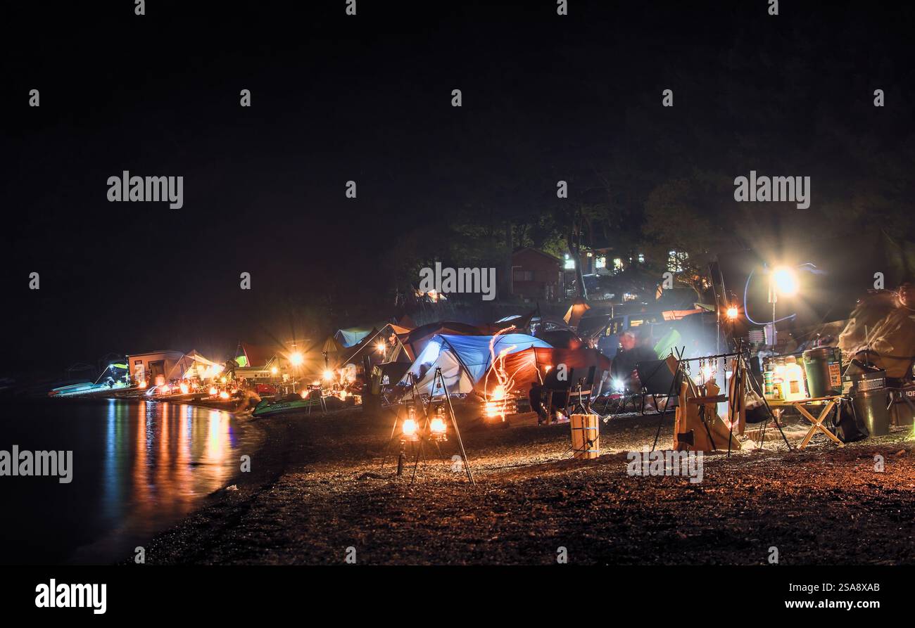 Long exposure at night of a well-lit line of campsites along the shore of a lake Stock Photo