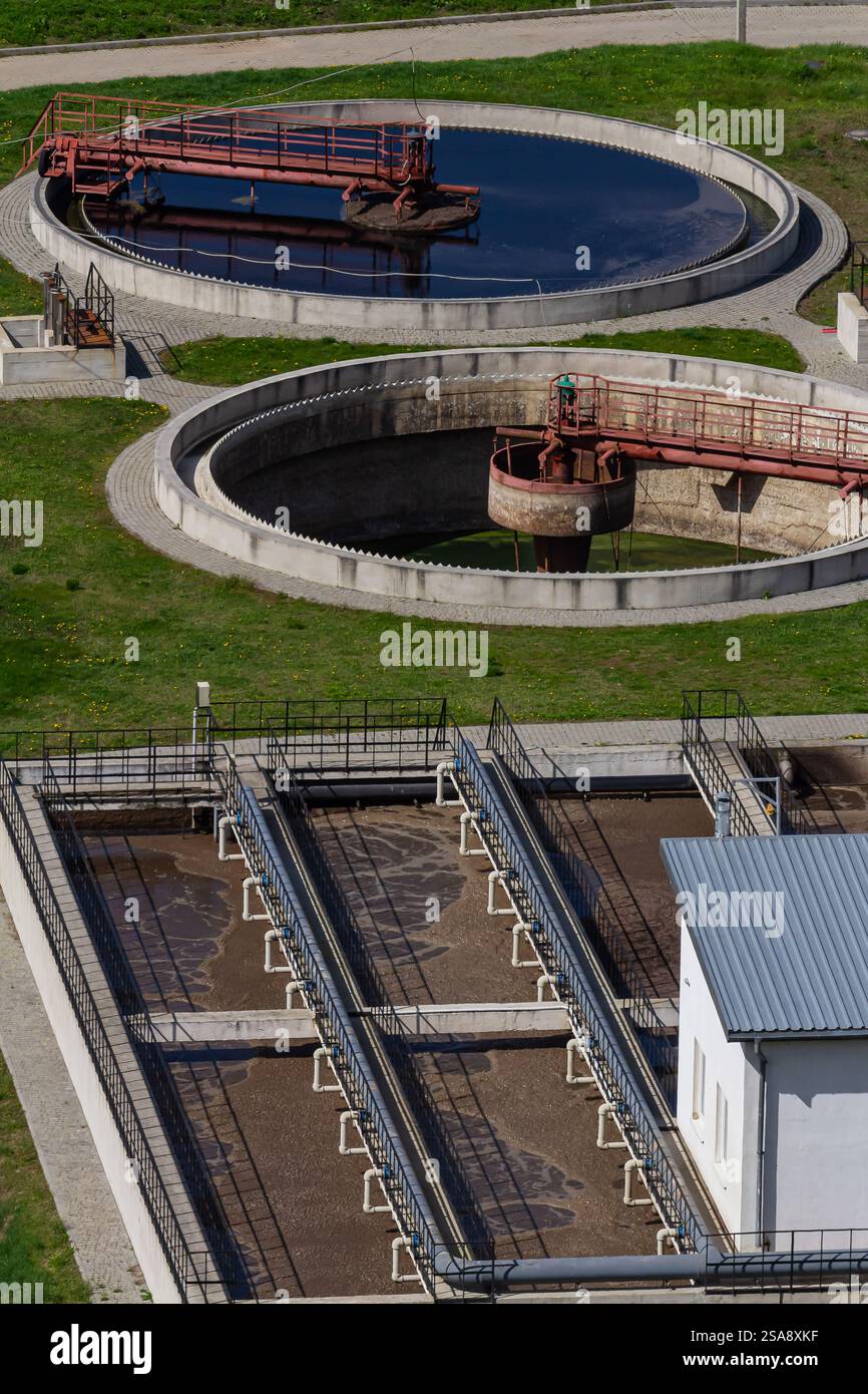 A water treatment facility features circular purification tanks and rectangular filtration units. Workers are present, maintaining and overseeing the Stock Photo