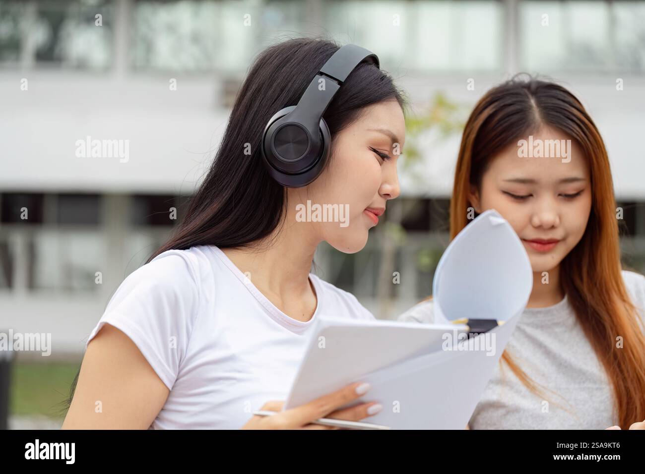 Focused students collaborating with headphones and study materials outdoors Stock Photo