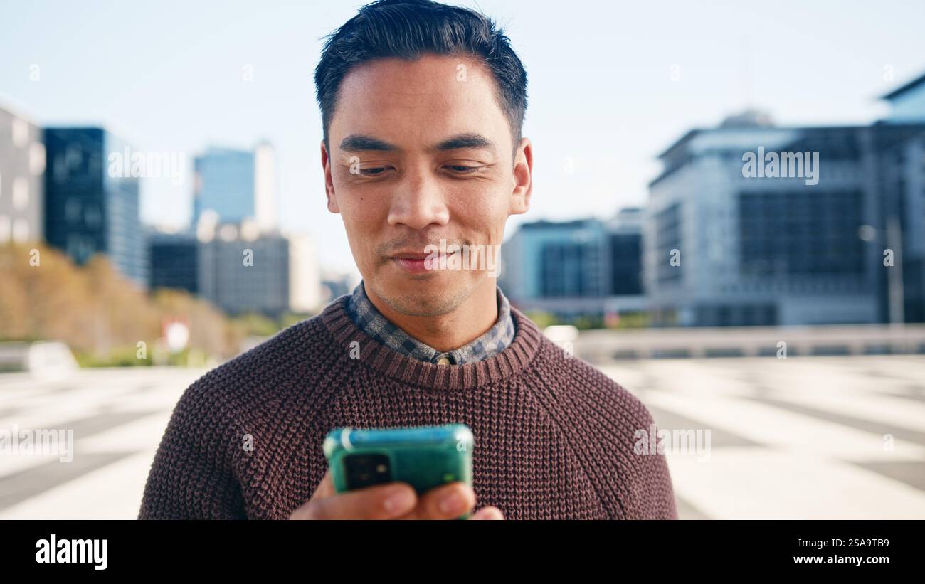 Young Man Smiling While Using Smartphone Outdoors in the City Stock Photo