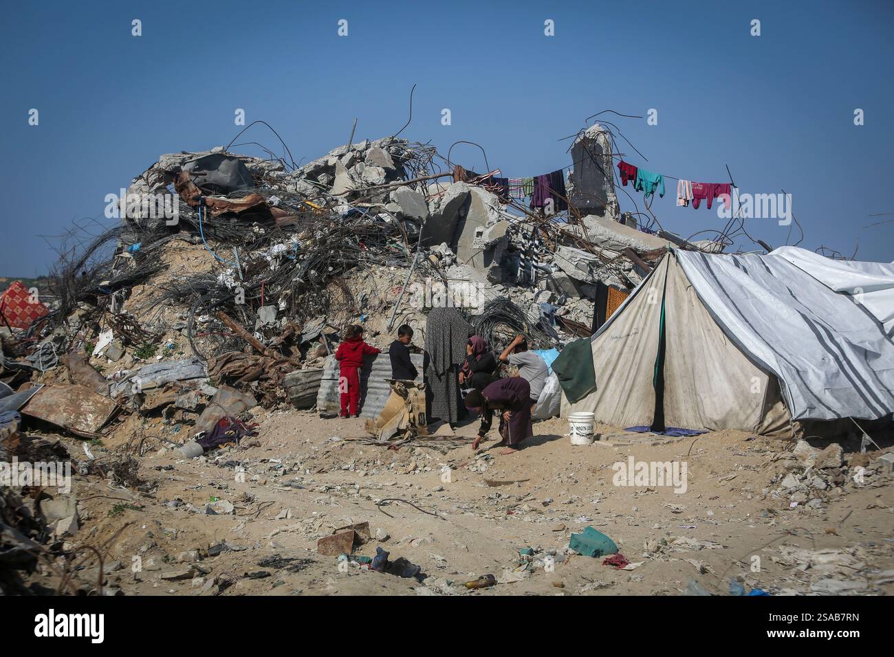 A Palestinian family sits outside a tent next to their destroyed house ...