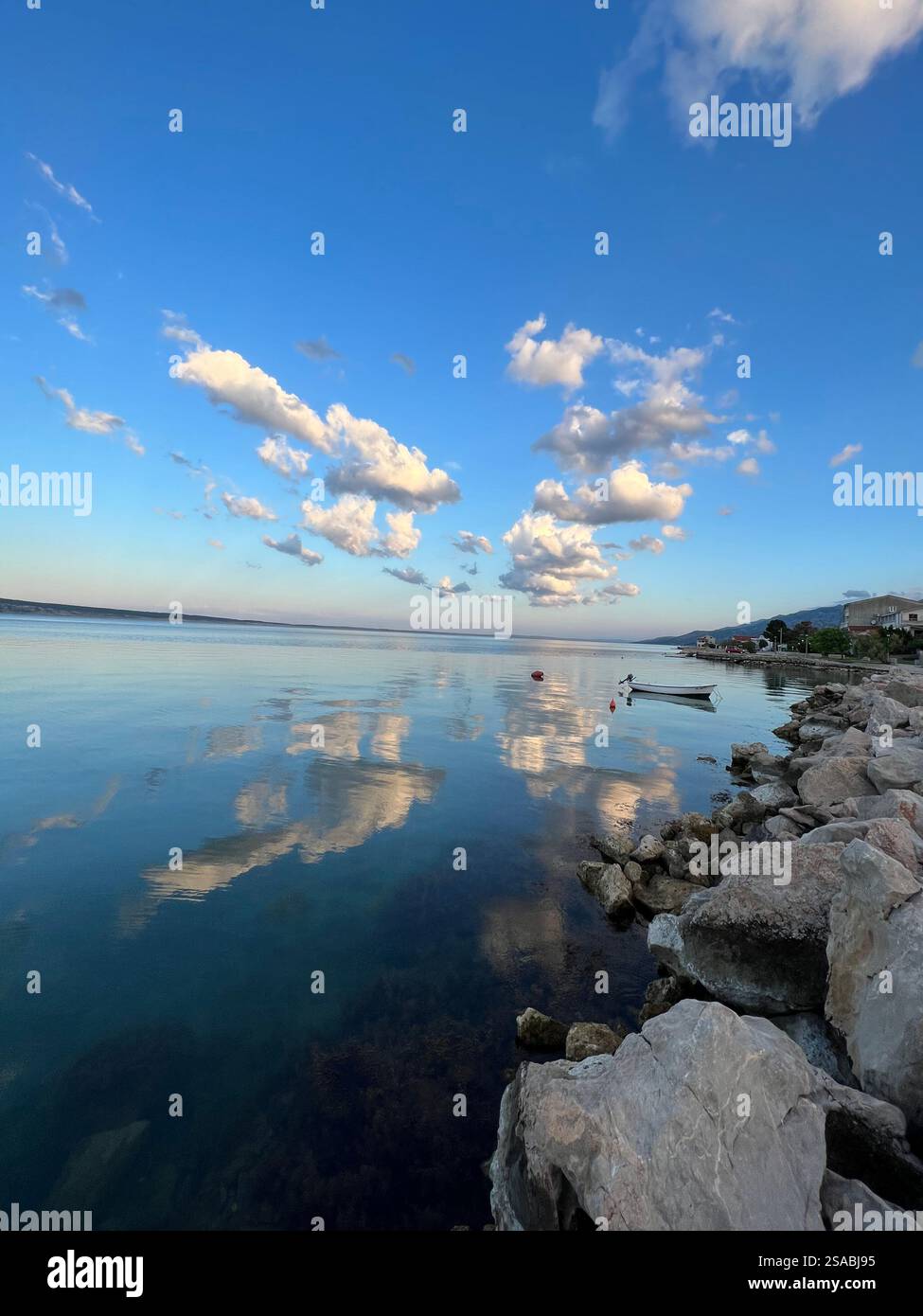 Tranquil waterfront scene with soft clouds reflected on calm blue waters at sunset - Smartphone Captured Stock Image