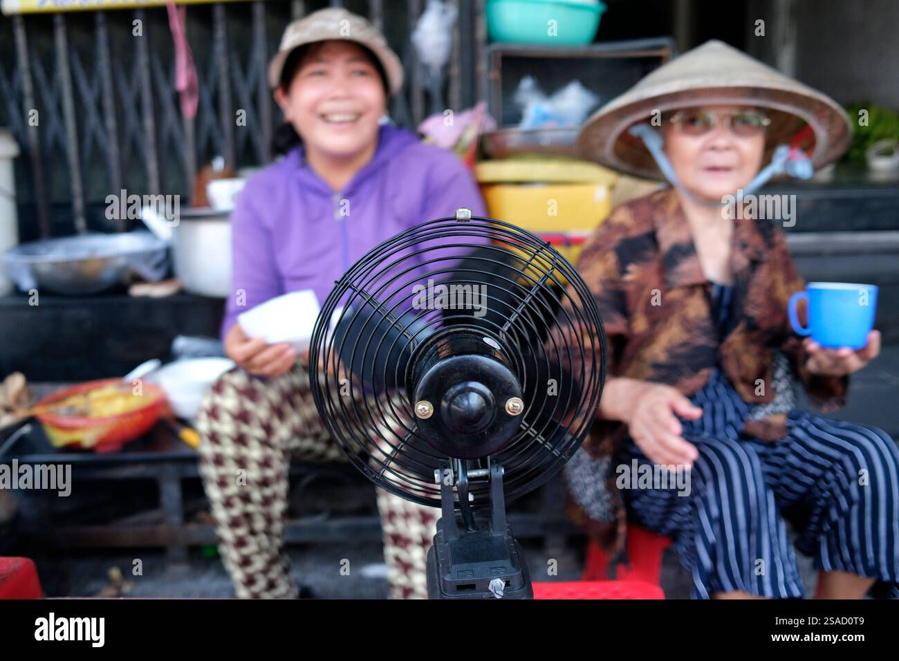 Two Vietnamese women enjoying the coolness of a fan.  Hue. Vietnam. Stock Photo