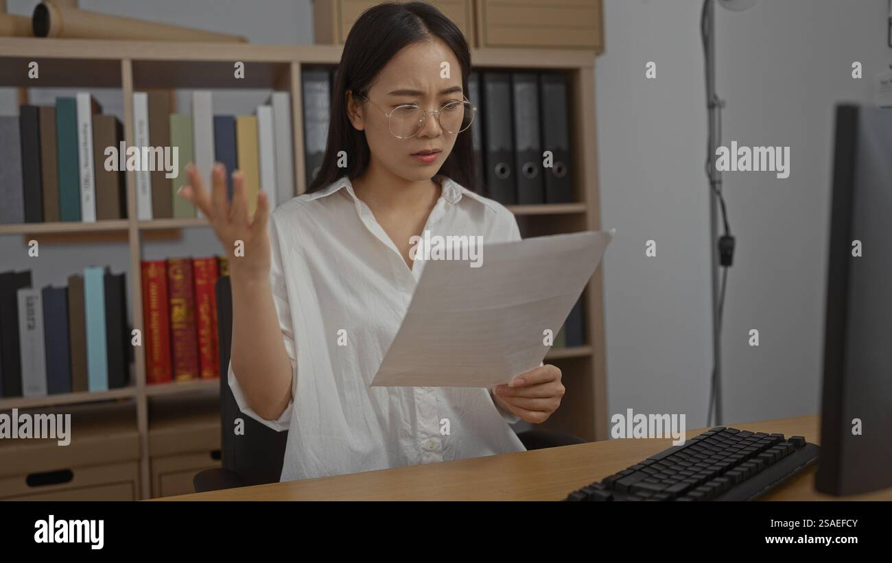 Young, chinese, woman in an office looking concerned while reading a ...