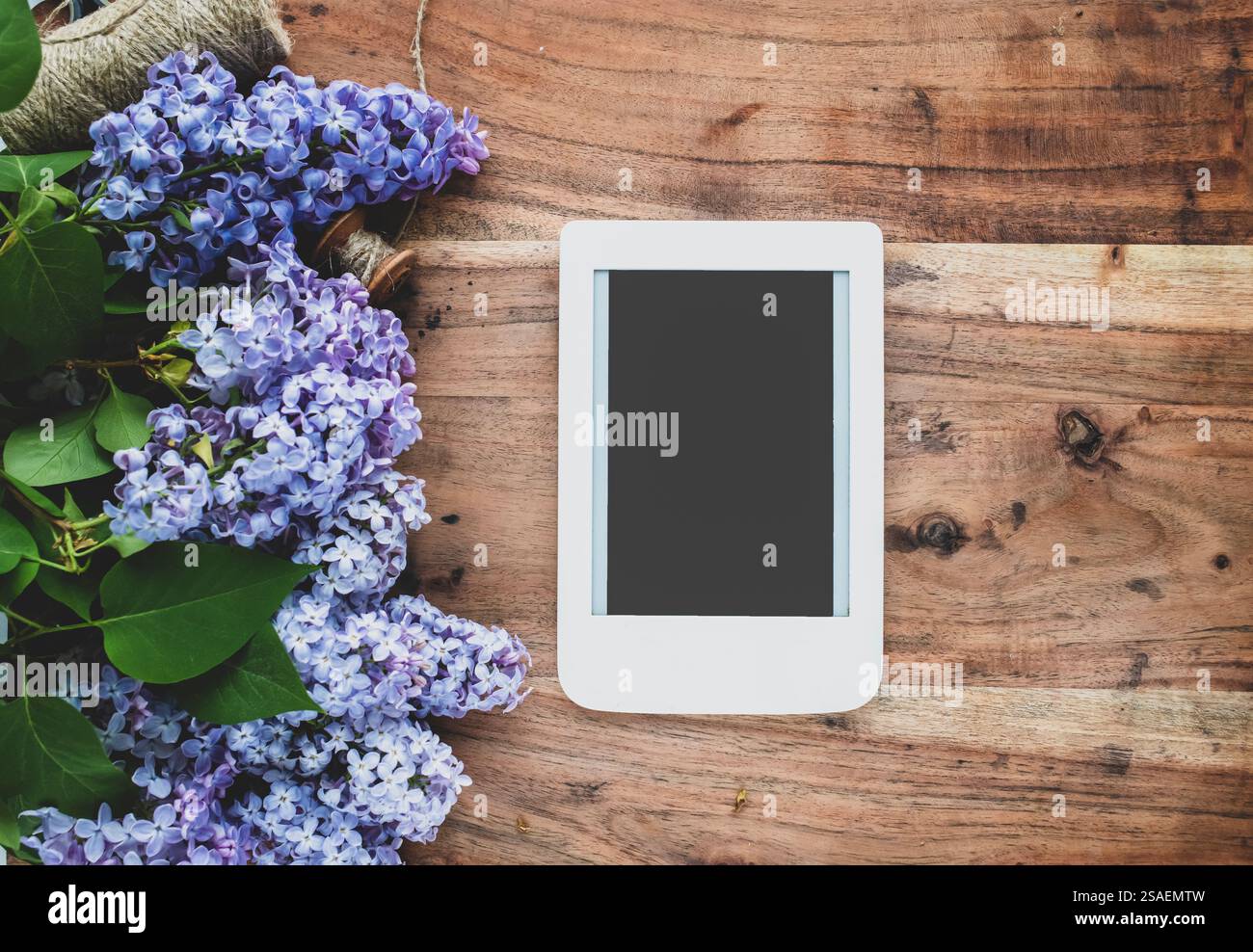 E-book on wooden background with lilac branches. Flat lay, top view. Template for feminine blog social media. Stock Photo