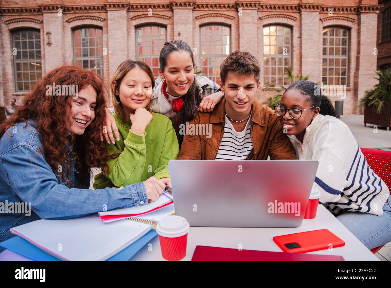 Enthusiastic Students Collaborating on a Laptop While Studying Together and Sharing Ideas in a Bright and Engaging Learning Environment Surrounded by Friends and Classmates at Their University Campus. High quality photo Stock Photo
