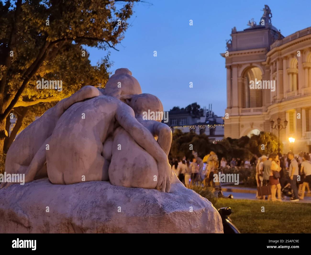 Sculpture-fountain "Youth" a.k.a. Children and the Frog or Narcissus in front of the opera of Odesa / Odessa seen from the back in evening; conceptual - Smartphone Captured Stock Image