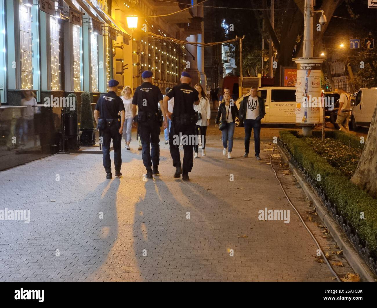 Ukrainian National guard walking on a street in Odesa / Odessa, Ukraine in the evening, with other pedestrians on the sidewalk - Smartphone Captured Stock Image