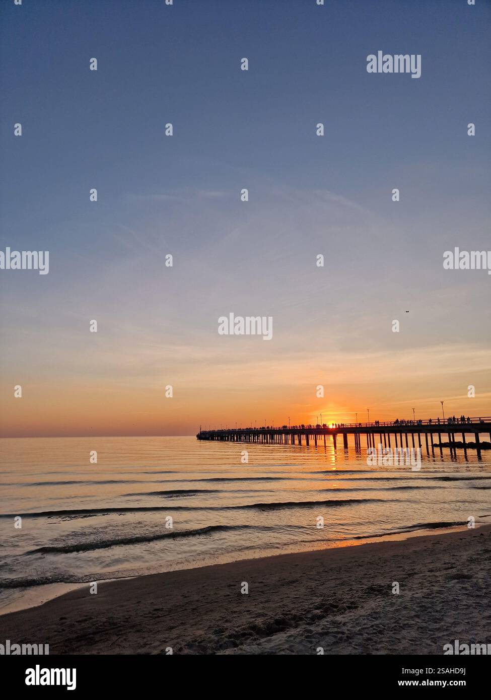 Serene sunset over a calm ocean or sea with a wooden pier, Baltic sea, Lithuania. Peaceful, tranquil scene, warm hues of orange and pink Stock Photo