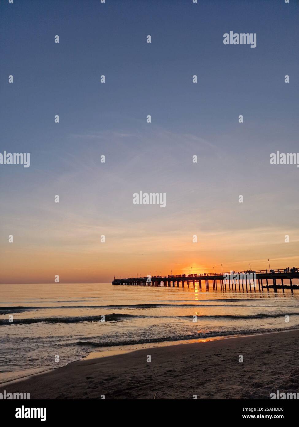Serene sunset over a calm ocean or sea with a wooden pier, Baltic sea, Lithuania. Peaceful, tranquil scene, warm hues of orange and pink Stock Photo