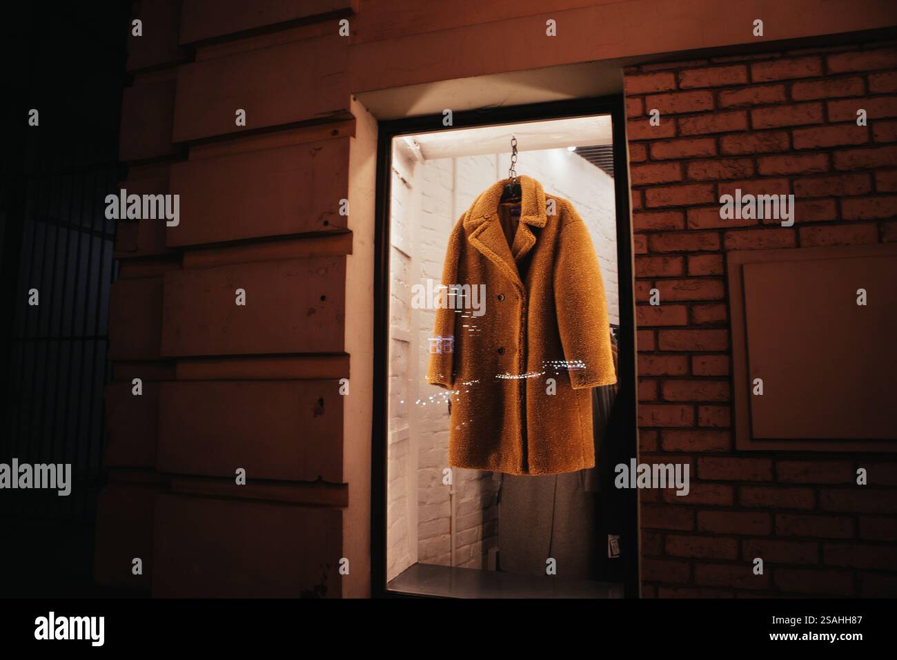 A brown faux fur coat hangs on hangers behind backlit glass in the ...