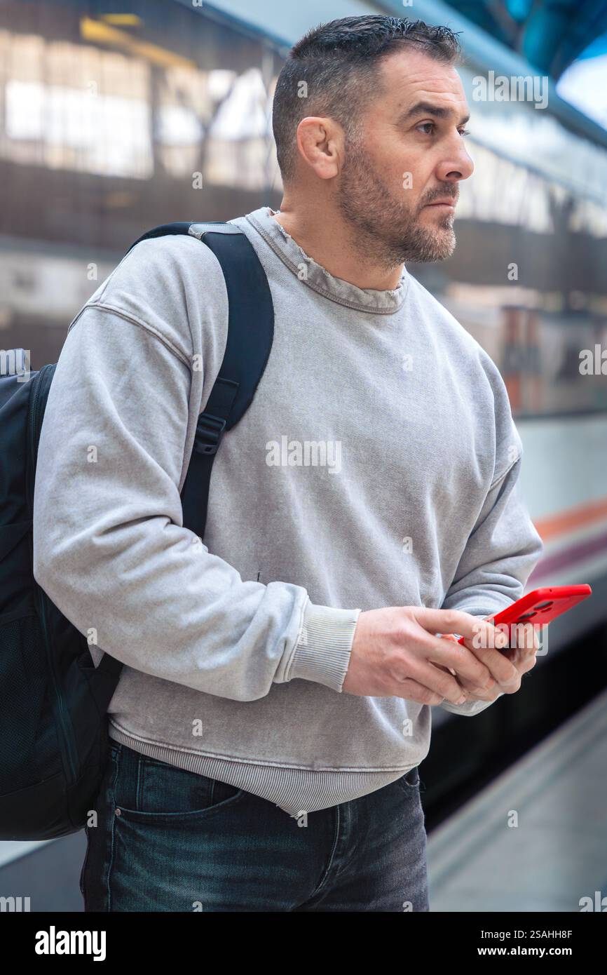 Focused Man with Backpack Using Smartphone at Train Station.Vertical Stock Photo
