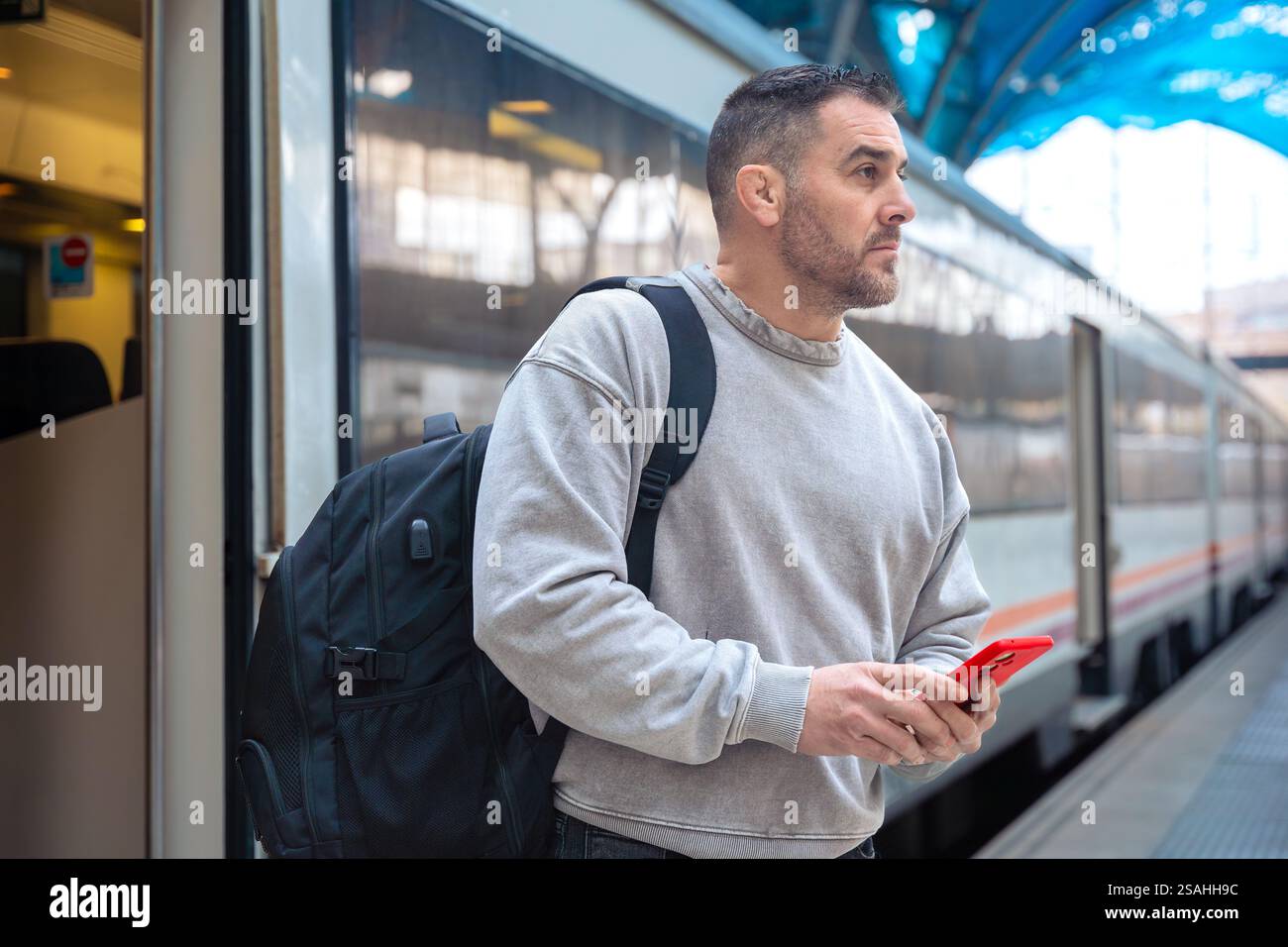 Focused Man with Backpack Using Smartphone at Train Station Stock Photo