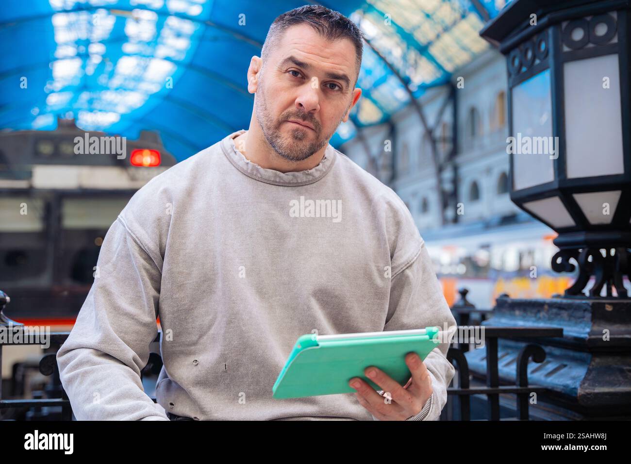 Focused Man Using Tablet While Waiting at Train Station Stock Photo