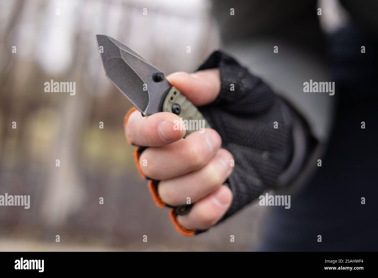 The man wearing tactical gloves using folding knife. Stock Photo